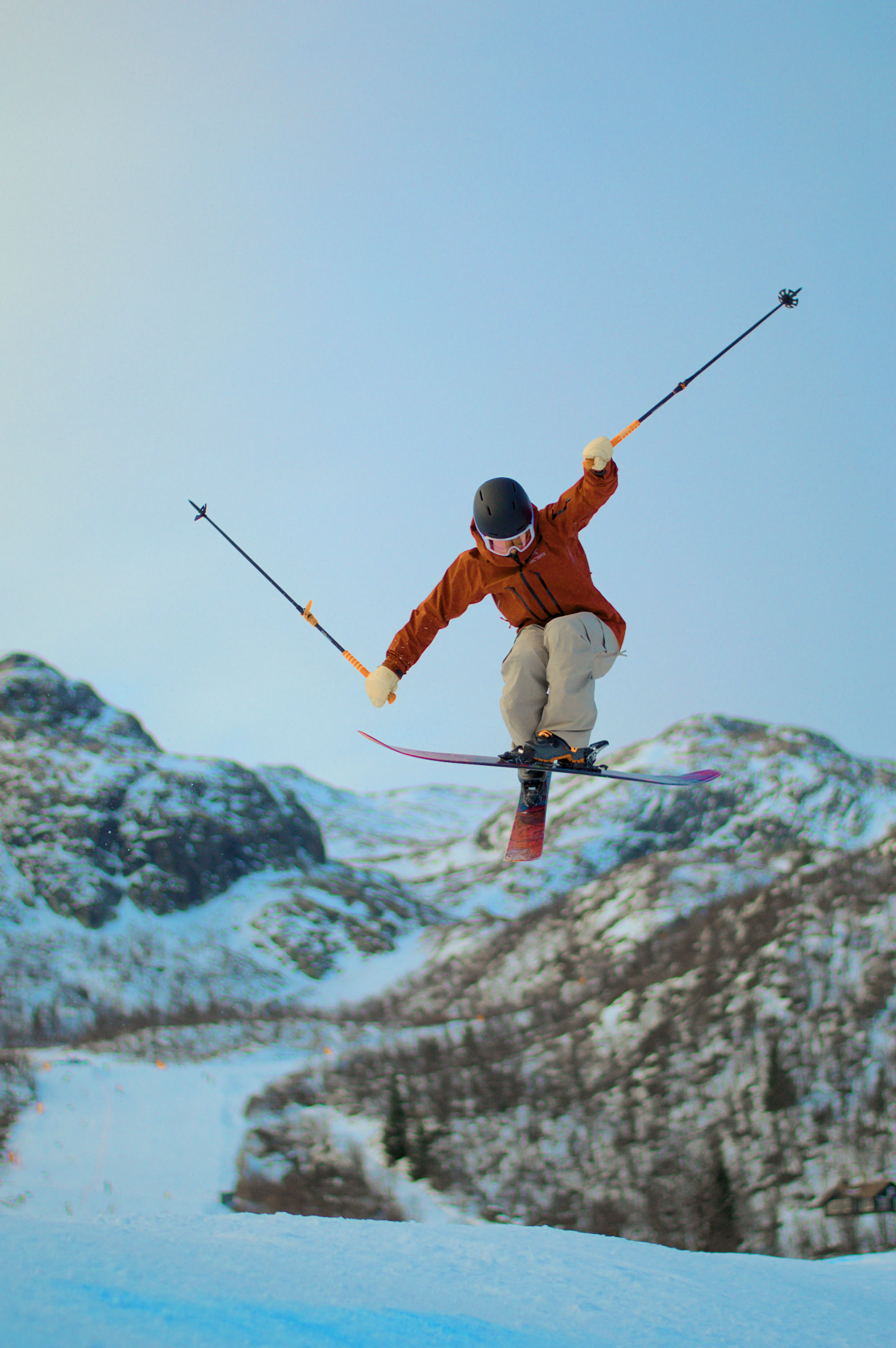 Skifahrer im Sprung mit gekreuzten Skiern vor Bergpanorama