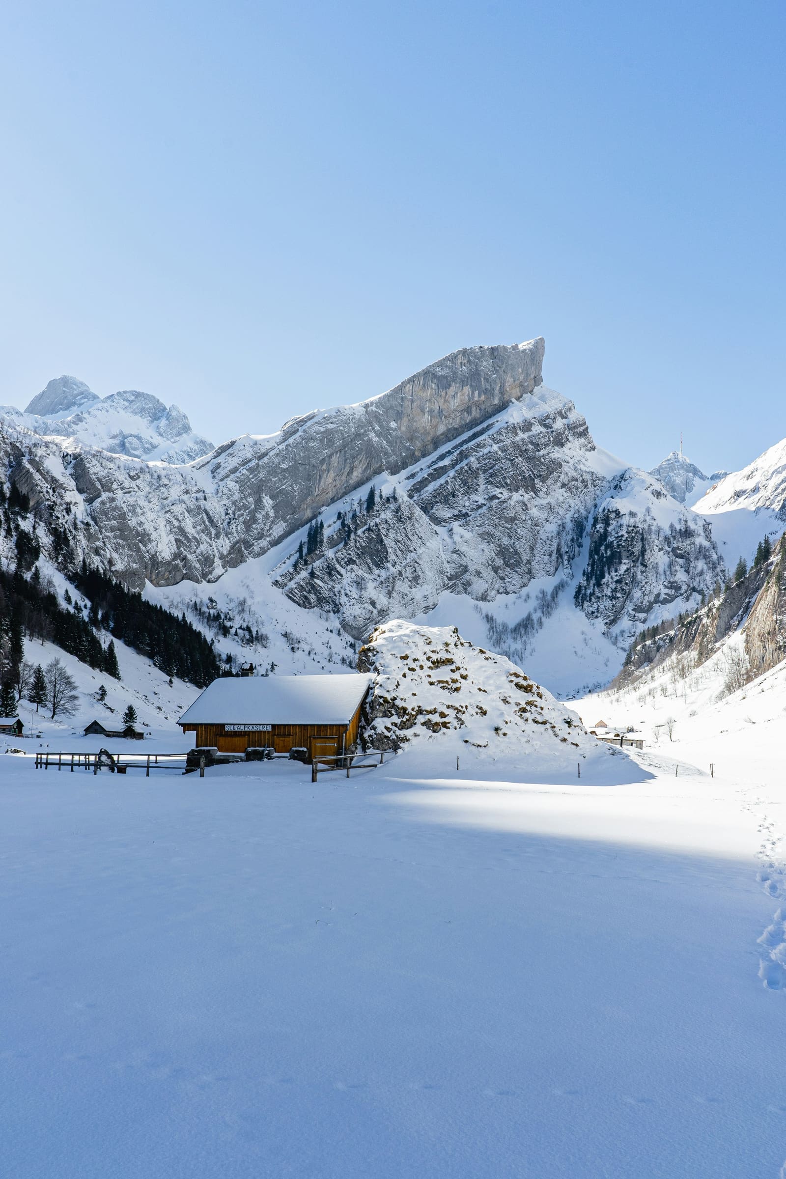 Verschneite Alphütte im Talboden unter steilen Kalkfelsen im Winter