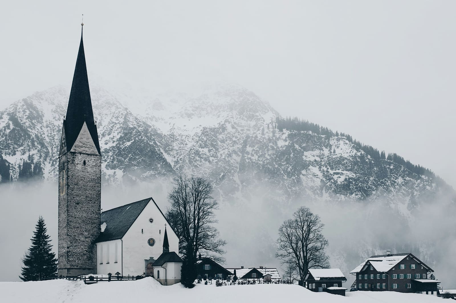 Verschneites Bergdorf mit spitzem Kirchturm vor nebelverhangenen Bergen