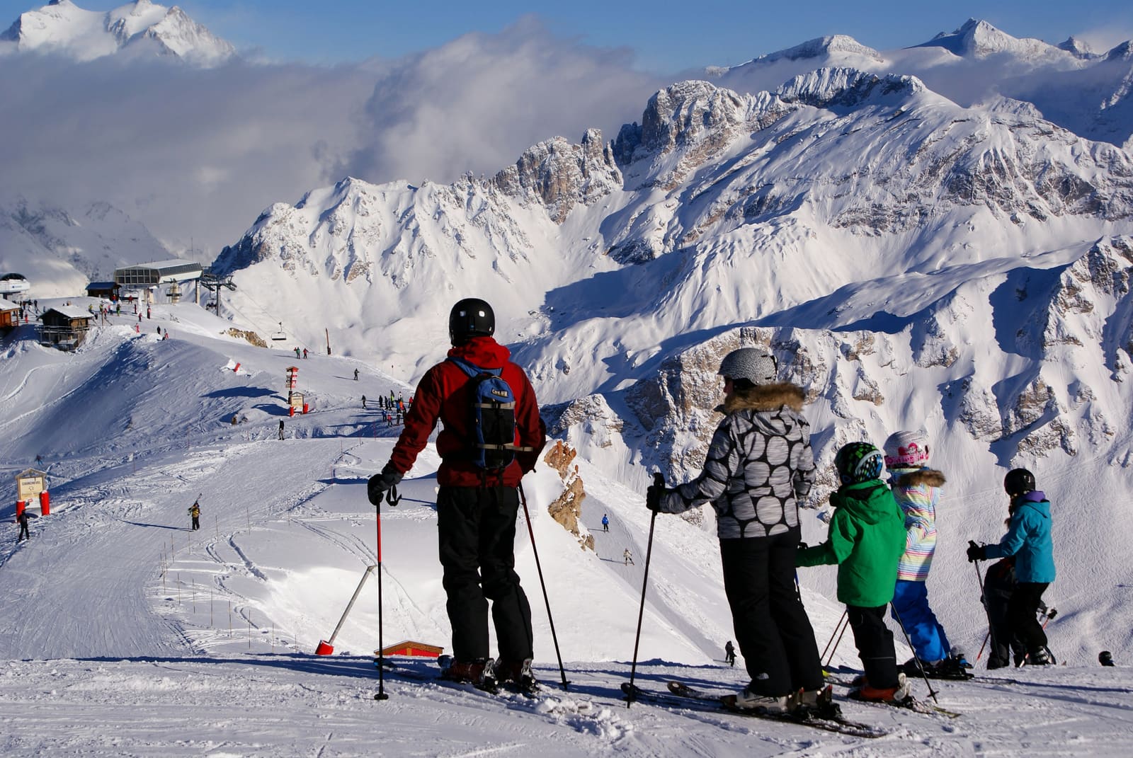 Familie auf Ski blickt vom Grat über das Skigebiet und felsige Gipfel