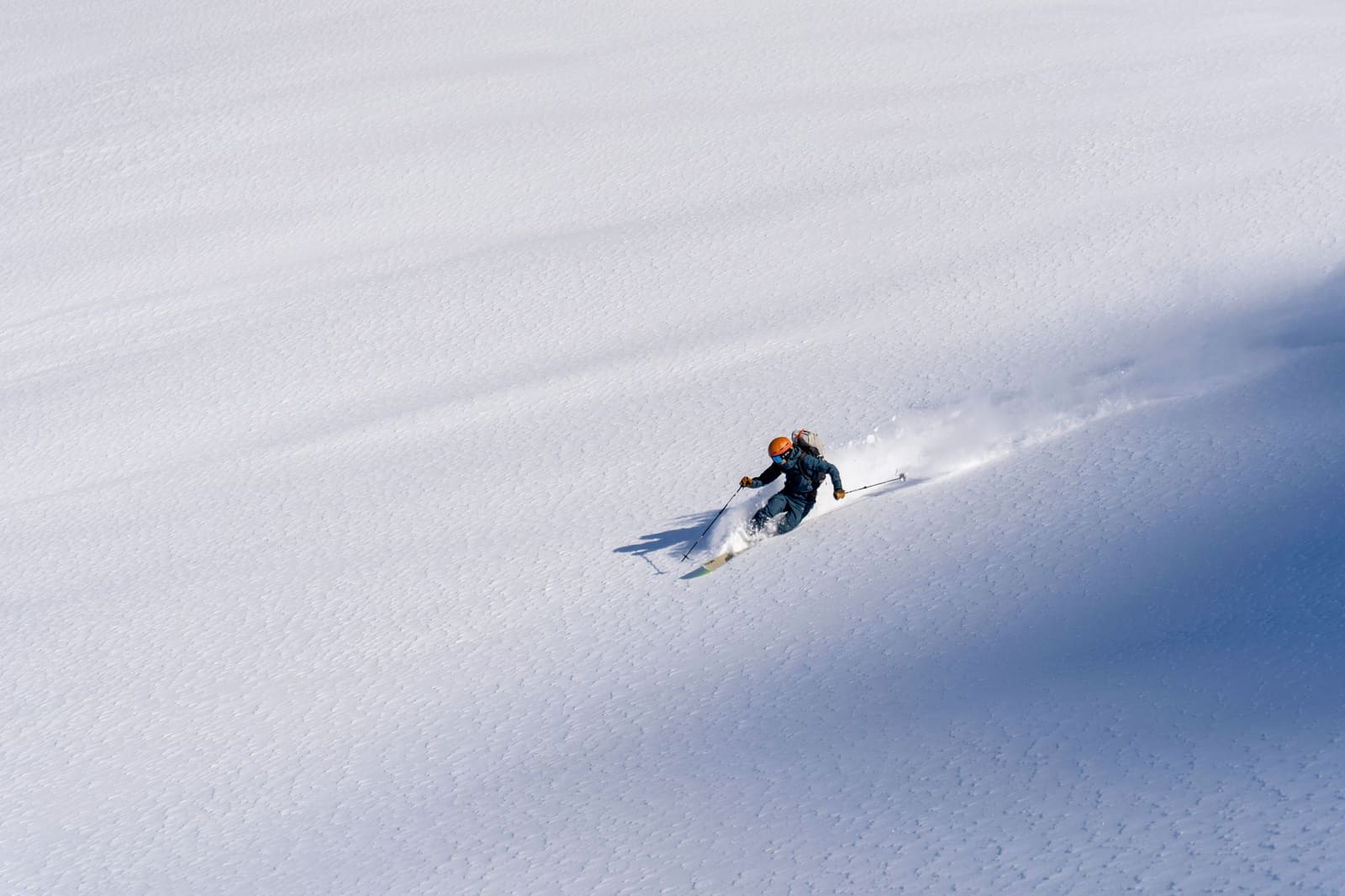 Skifahrerin zieht einen Pulverschneeschwung über einen weiten, unberührten Hang
