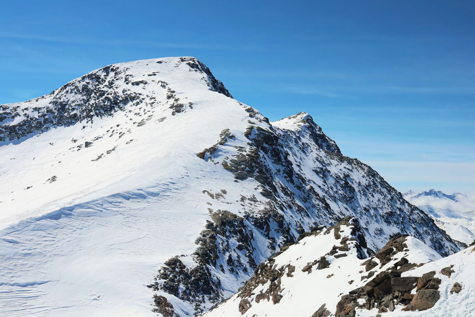 Verschneiter Felsgipfel mit Grat vor tiefblauem Himmel