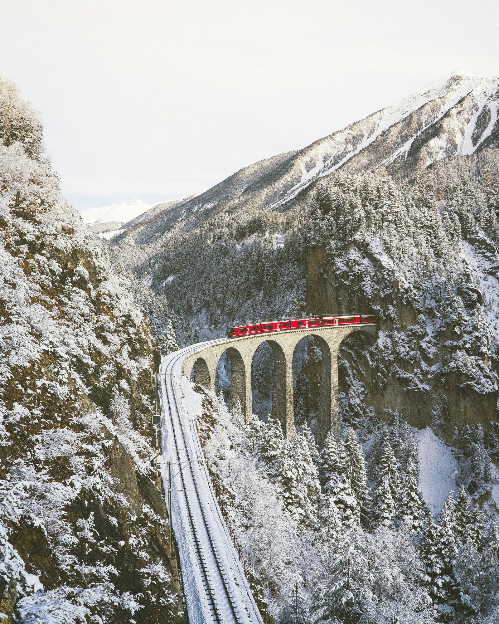 Roter Zug fährt über den verschneiten Landwasserviadukt im Albulatal