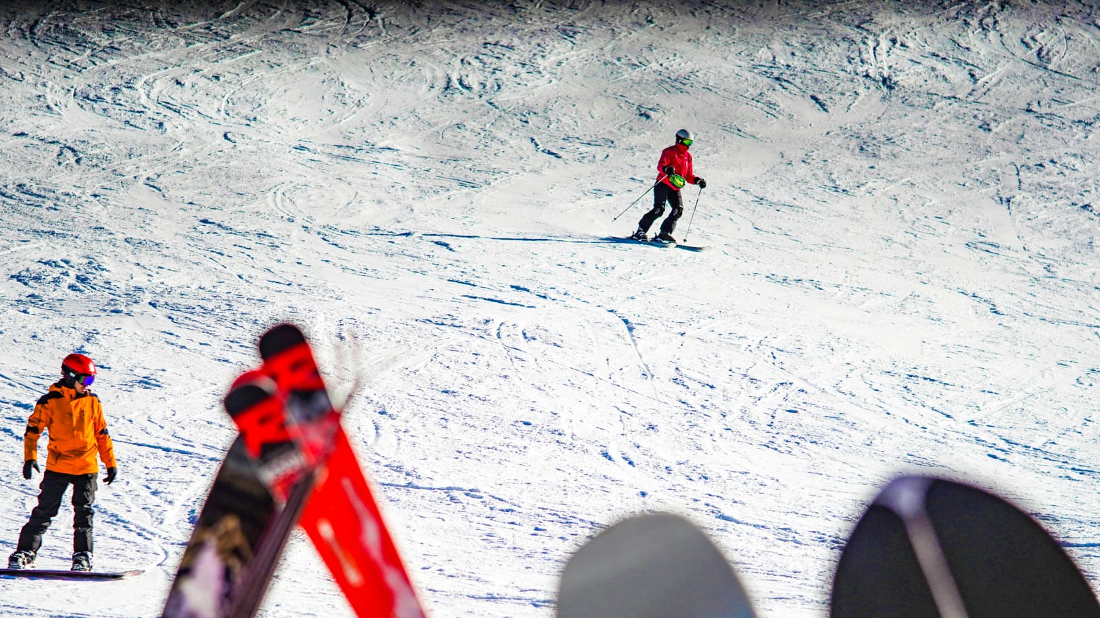 Skifahrer und Snowboarder auf sonniger Piste, unscharfe Ski im Vordergrund