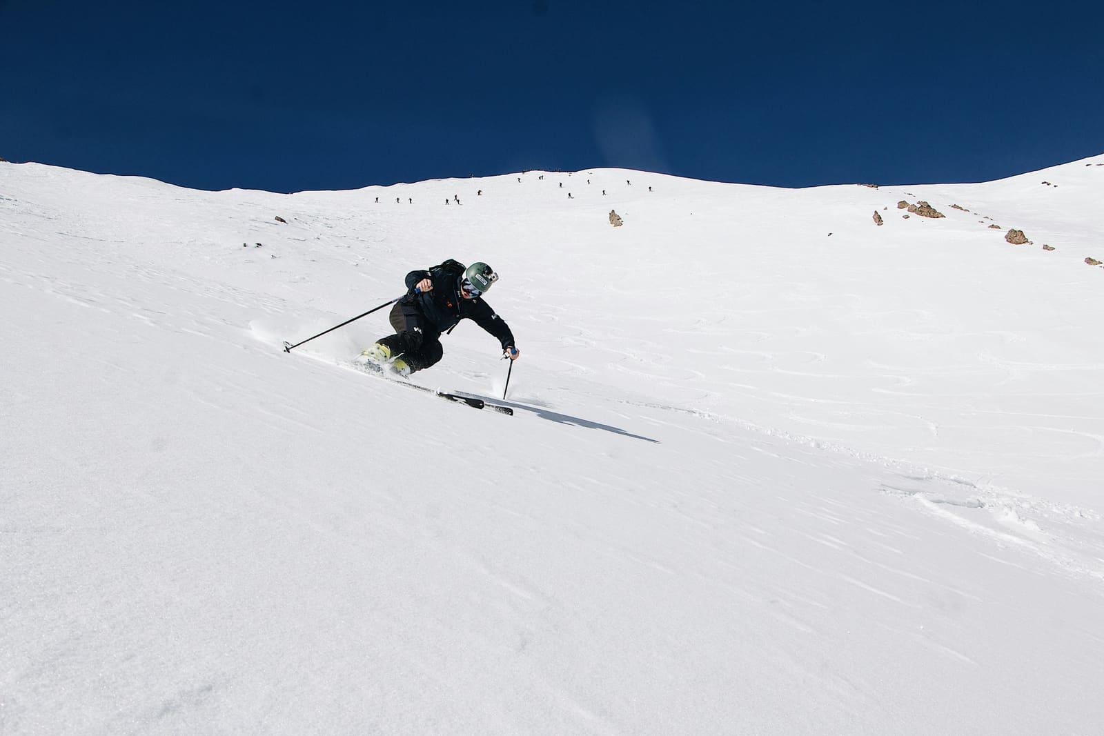 Skifahrer im Schwung an weitem Schneehang unter tiefblauem Himmel