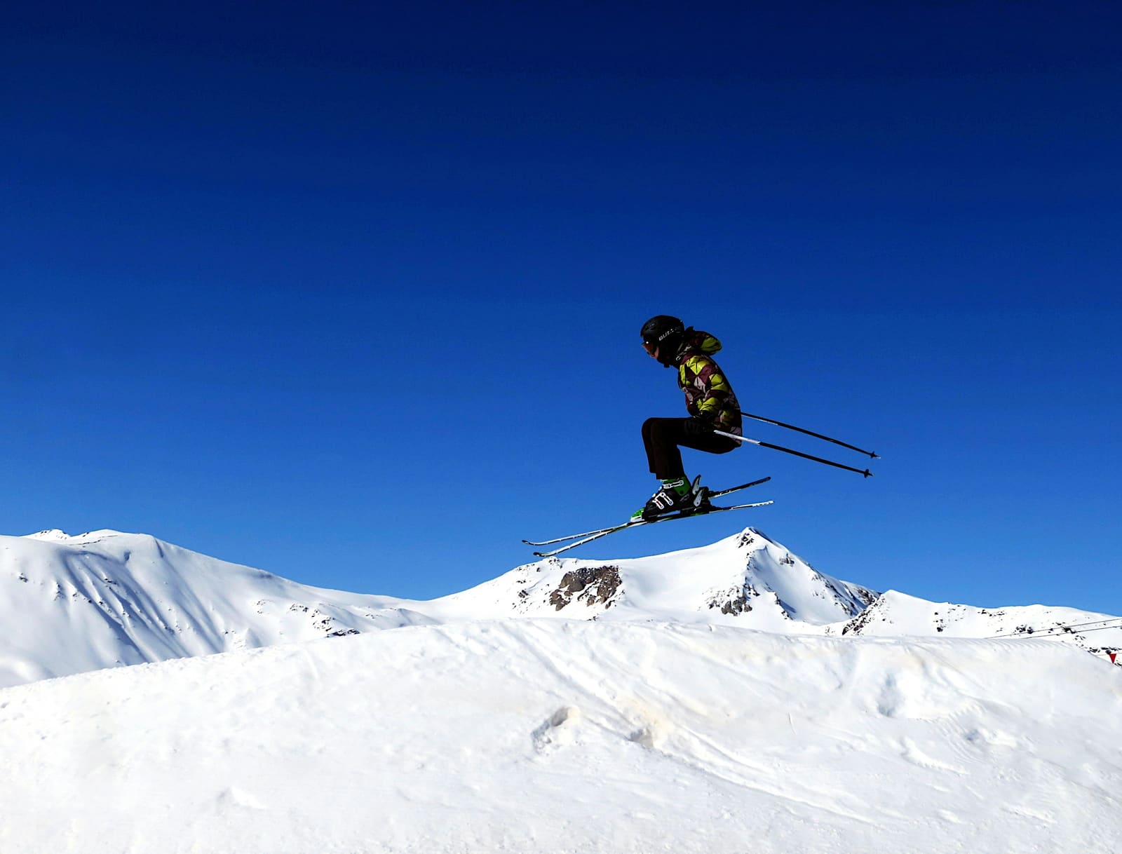 Junger Skifahrer springt vor tiefblauem Himmel über verschneite Gipfel