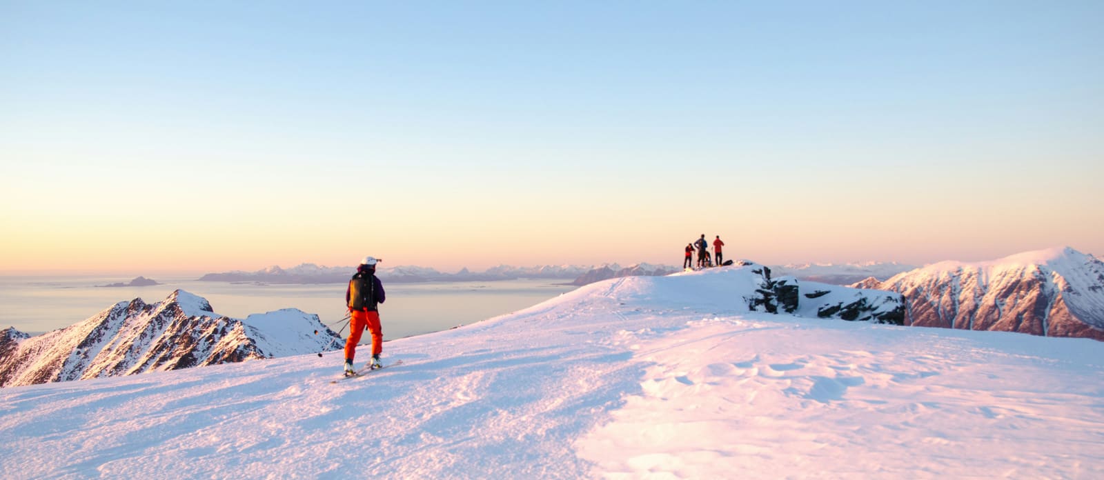 Skitourengeher auf einem Gipfelgrat im Abendlicht über einem Nebelmeer