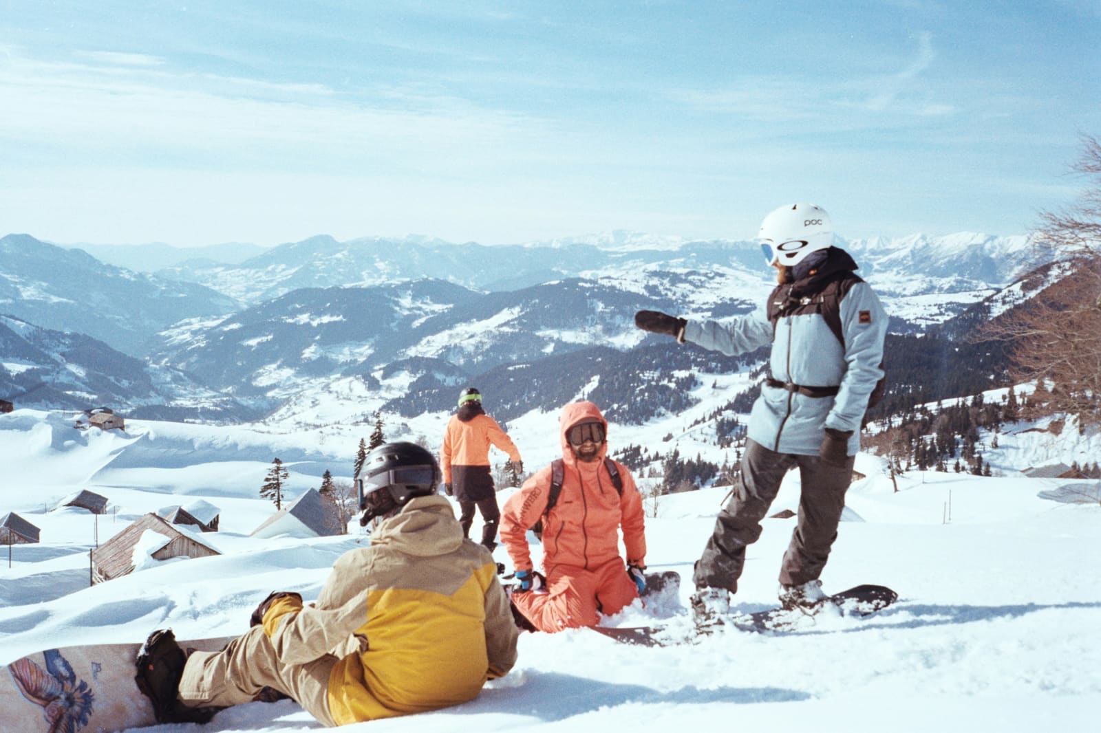 Snowboardgruppe macht Pause am Hang, eine Person steht und erklärt, dahinter weites Alpenpanorama