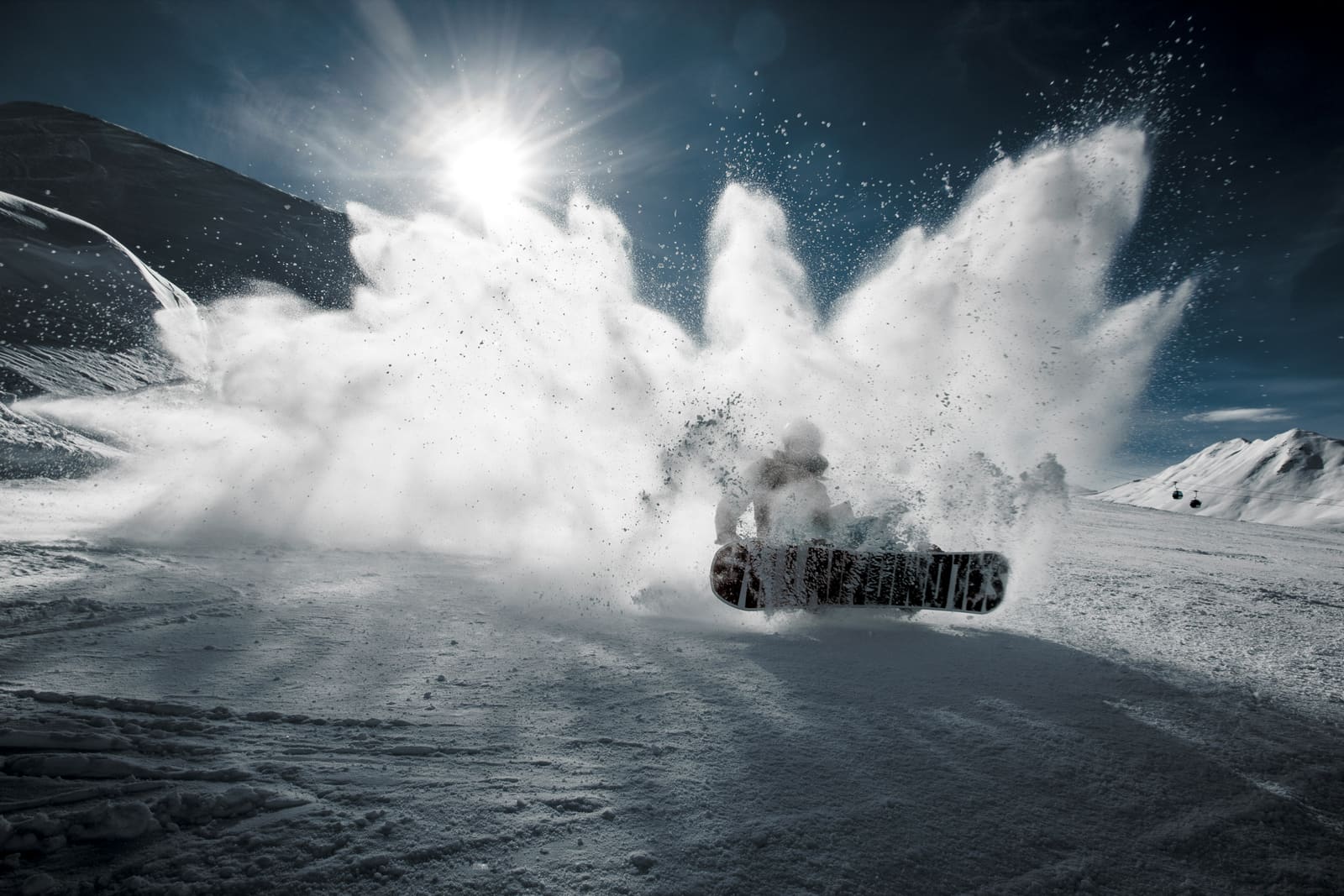 Snowboarder wirbelt im Gegenlicht eine grosse Schneewolke auf