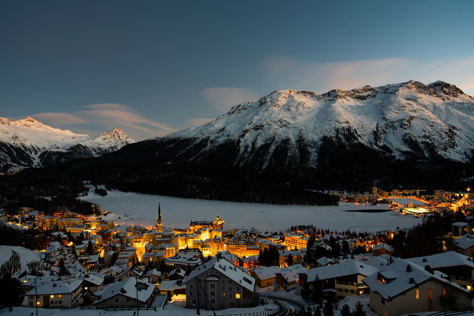 St. Moritz zur blauen Stunde mit beleuchtetem Ort und verschneiten Bergen