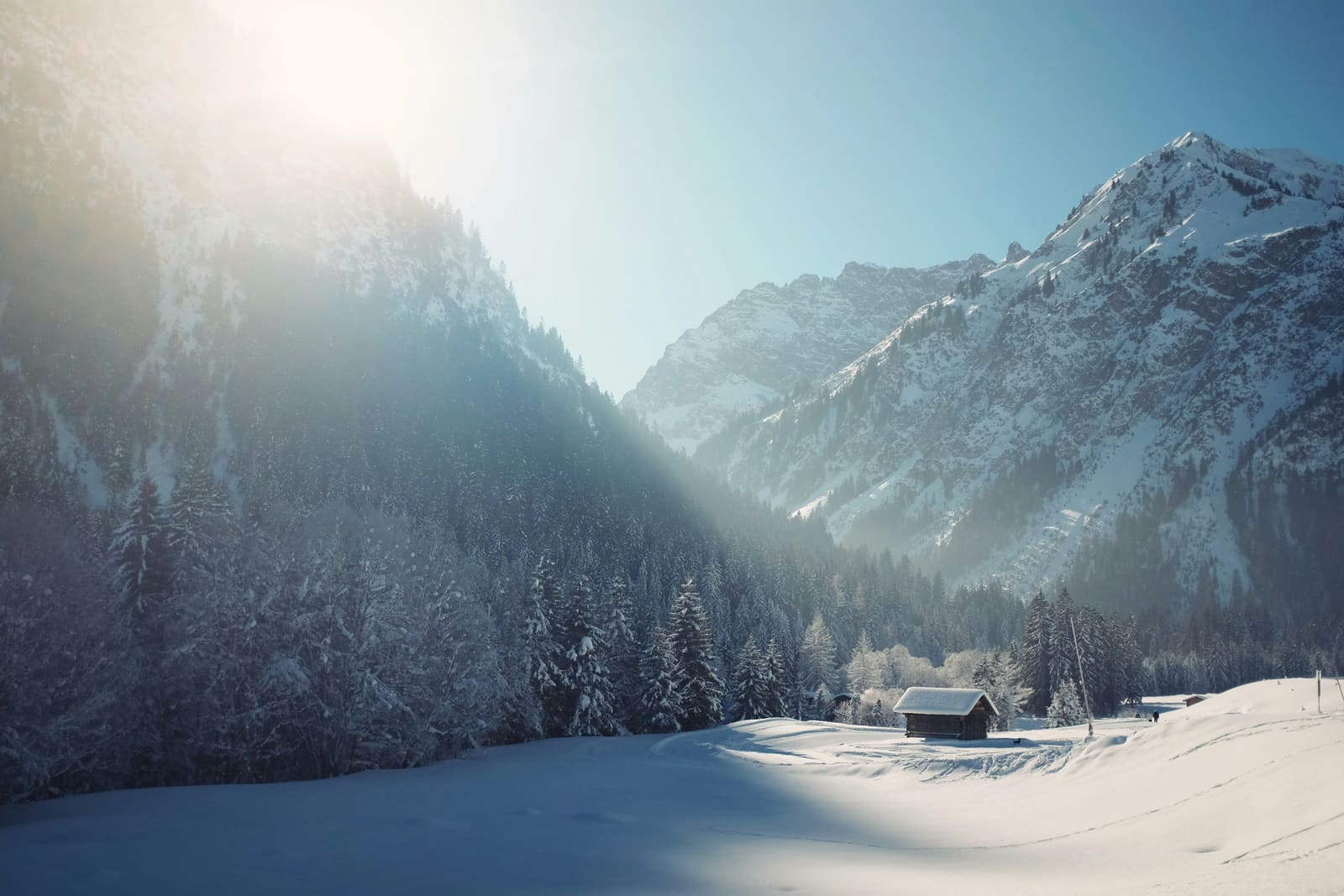 Verschneites Bergtal mit kleinem Stadel im Gegenlicht der Wintersonne