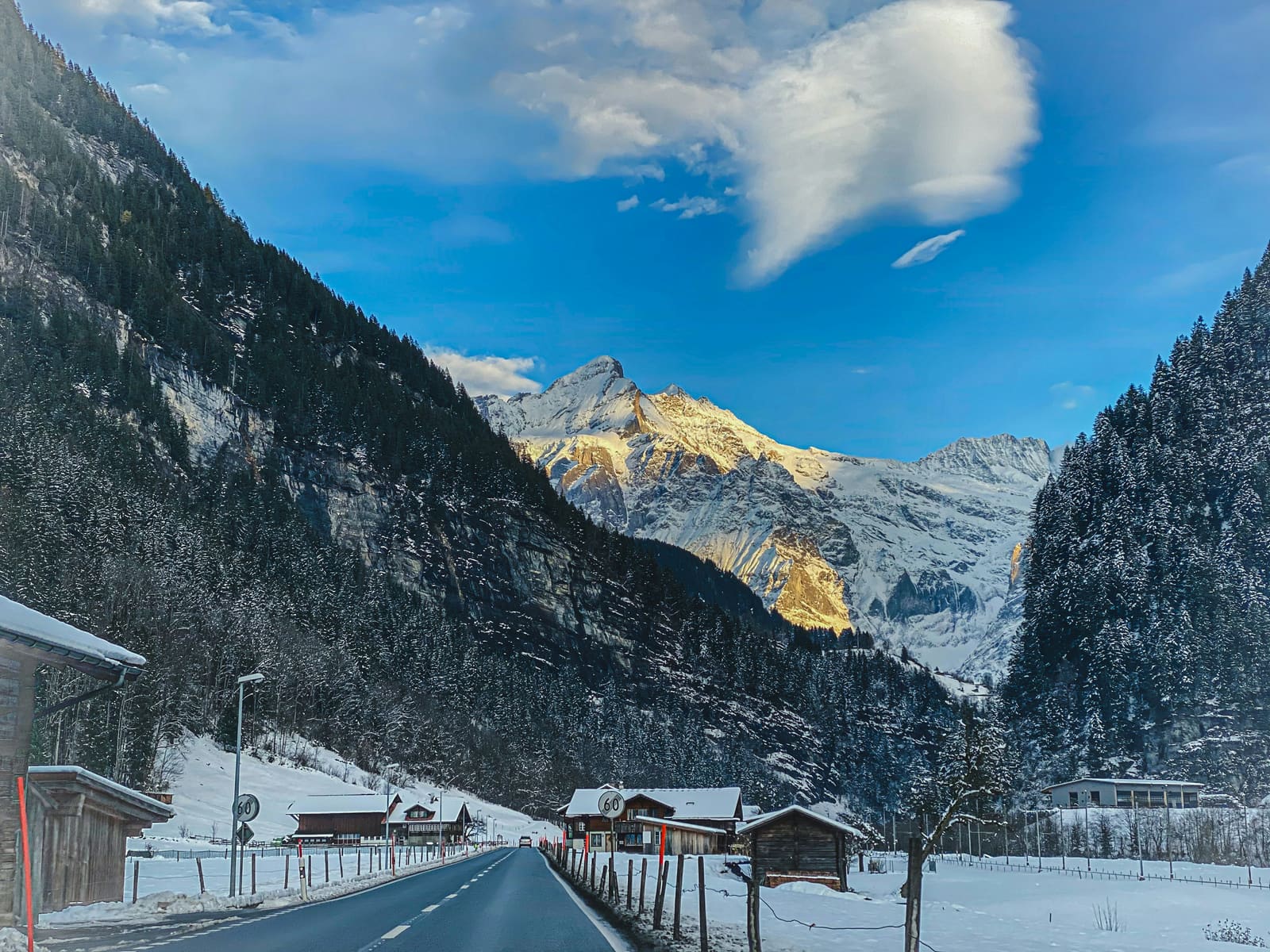 Strasse durch ein verschneites Bergtal mit Chalets und sonnenbeschienenem Gipfel